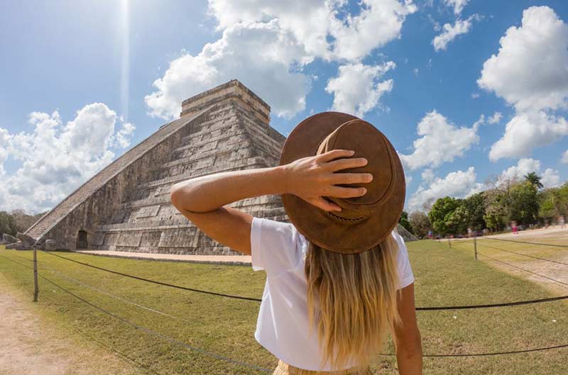 Woman holding her hat looking at a mexican pyramid